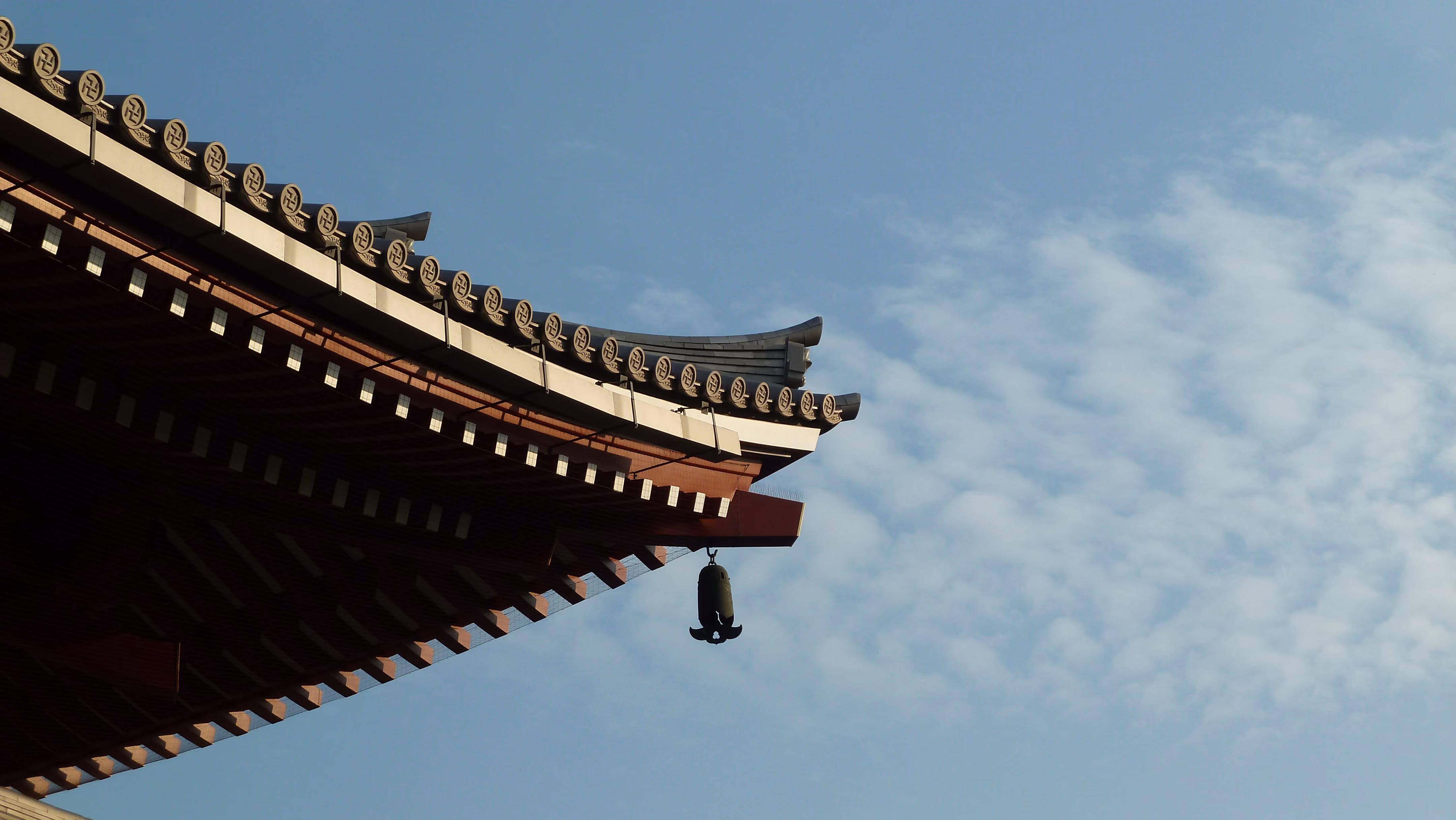 Detail of Senso-ji's roofline with a wind bell hanging from the eave against a blue sky