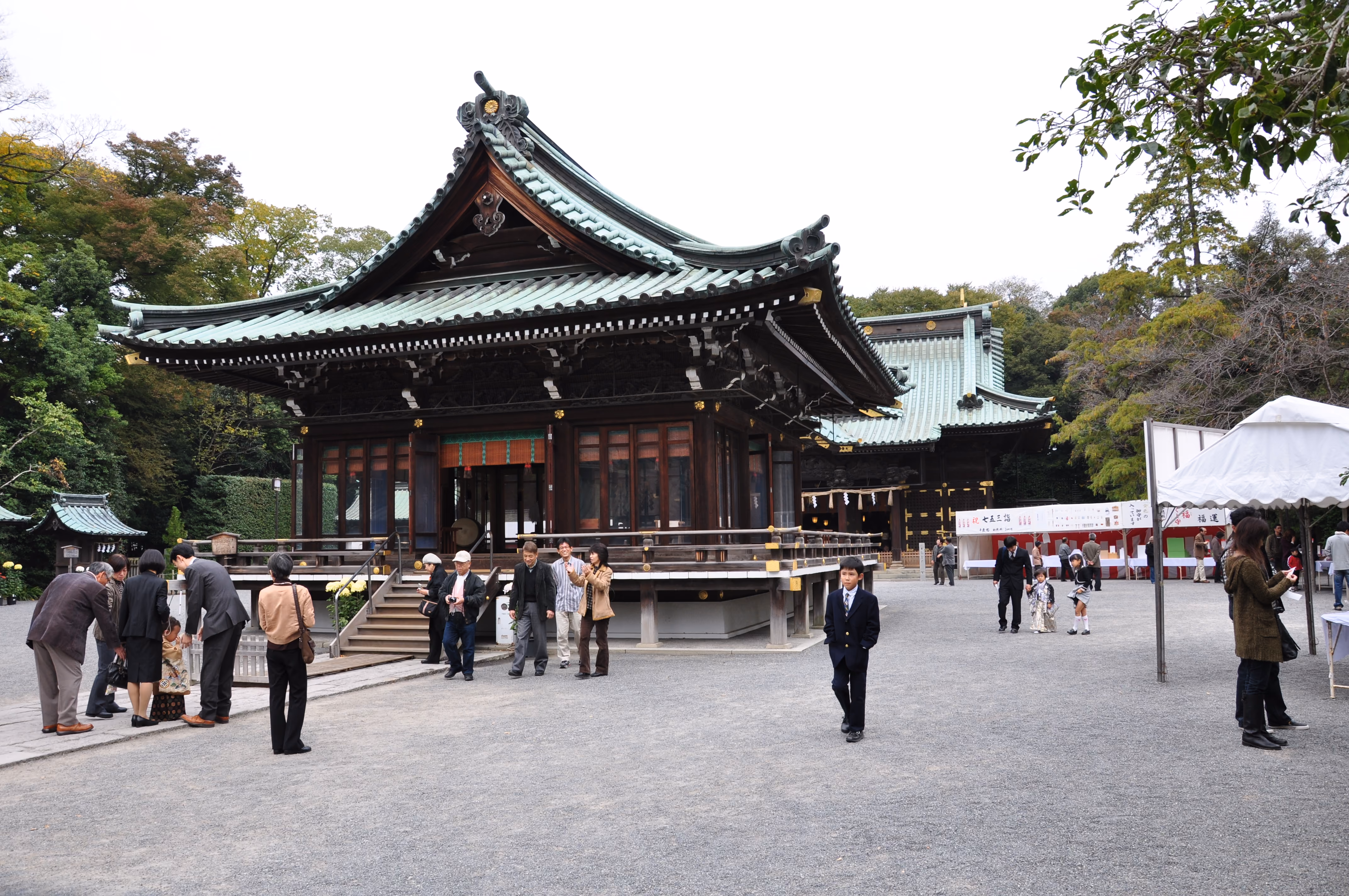 A family walking across the courtyard, a child pushing a tricycle, in front of Mishima Taisha's main hall