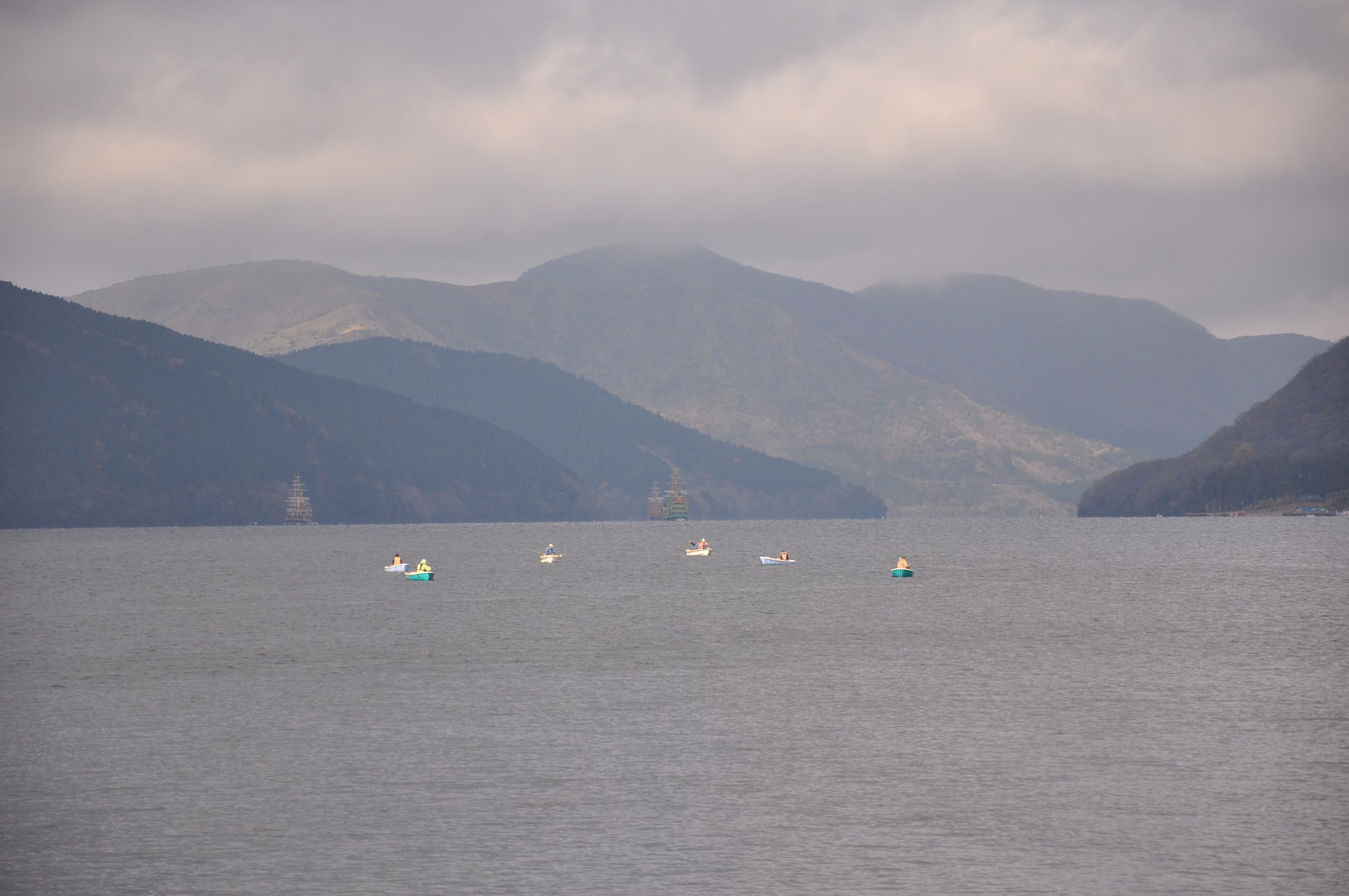 Rowboats scattered near the shore of Lake Ashi, with tour boats visible in the distance