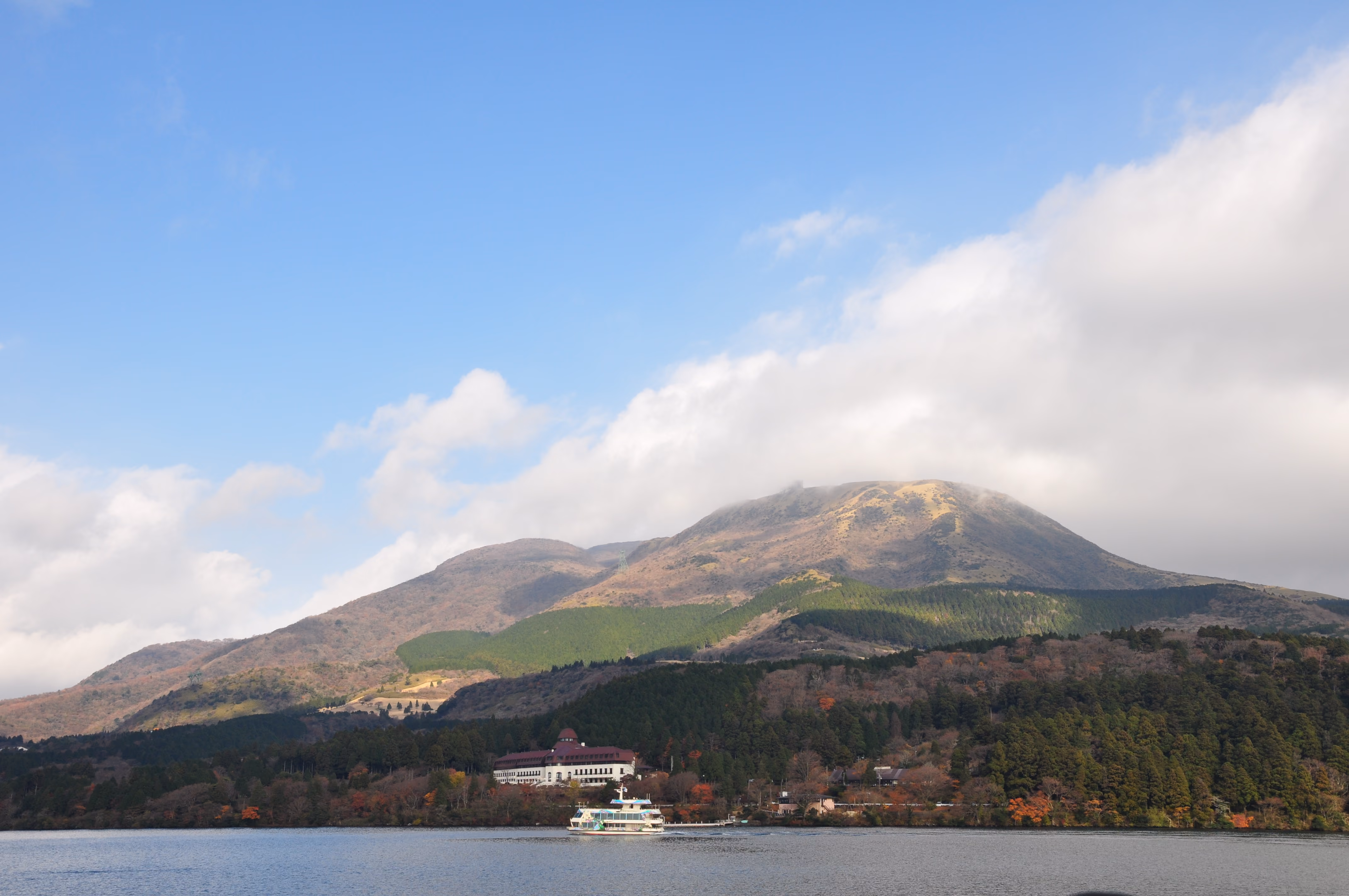 A white ferry boat approaching a lakeside hotel with a red roof at Lake Ashi
