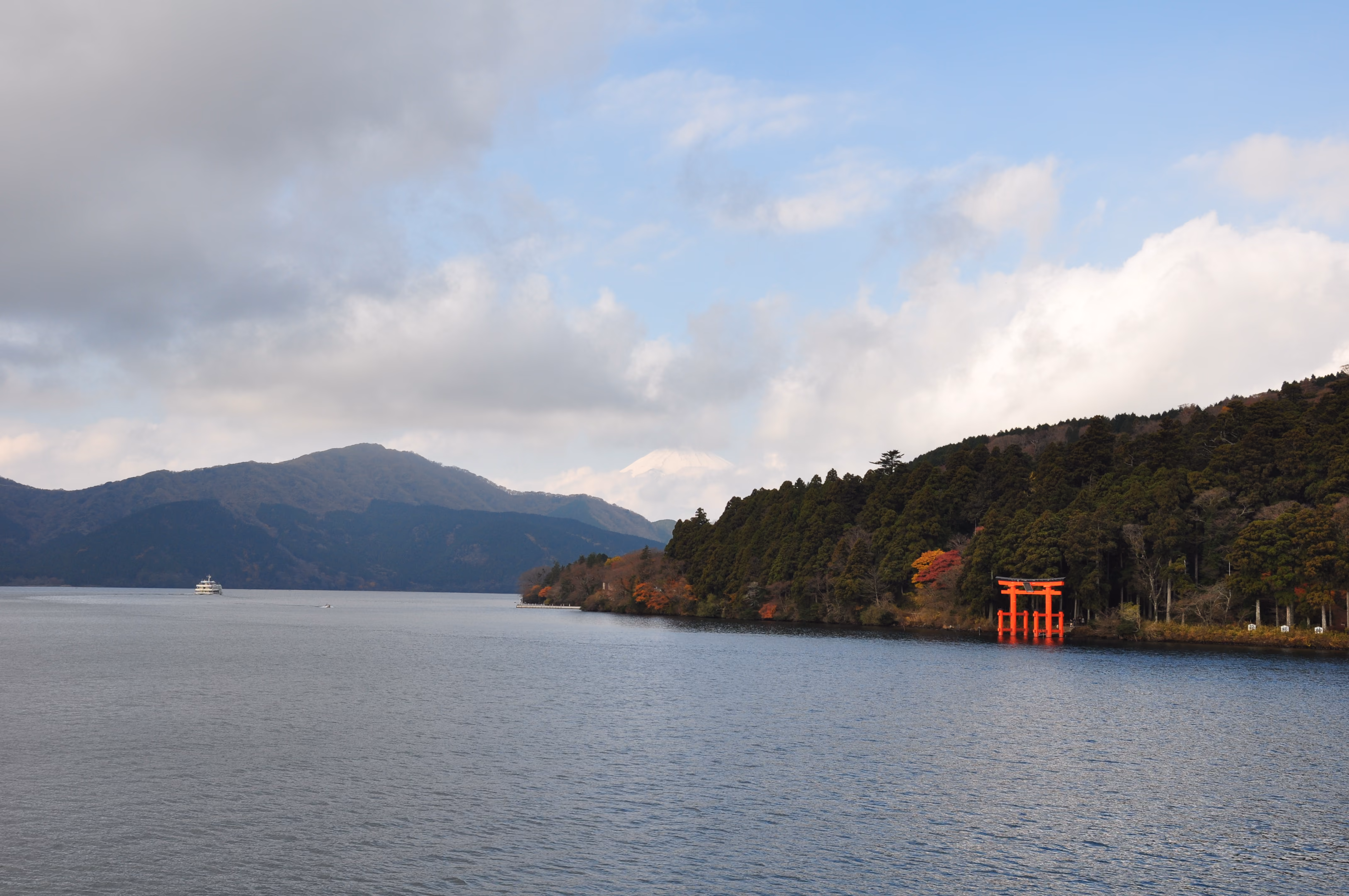 A red torii gate standing in Lake Ashi with Mount Fuji visible in the distance