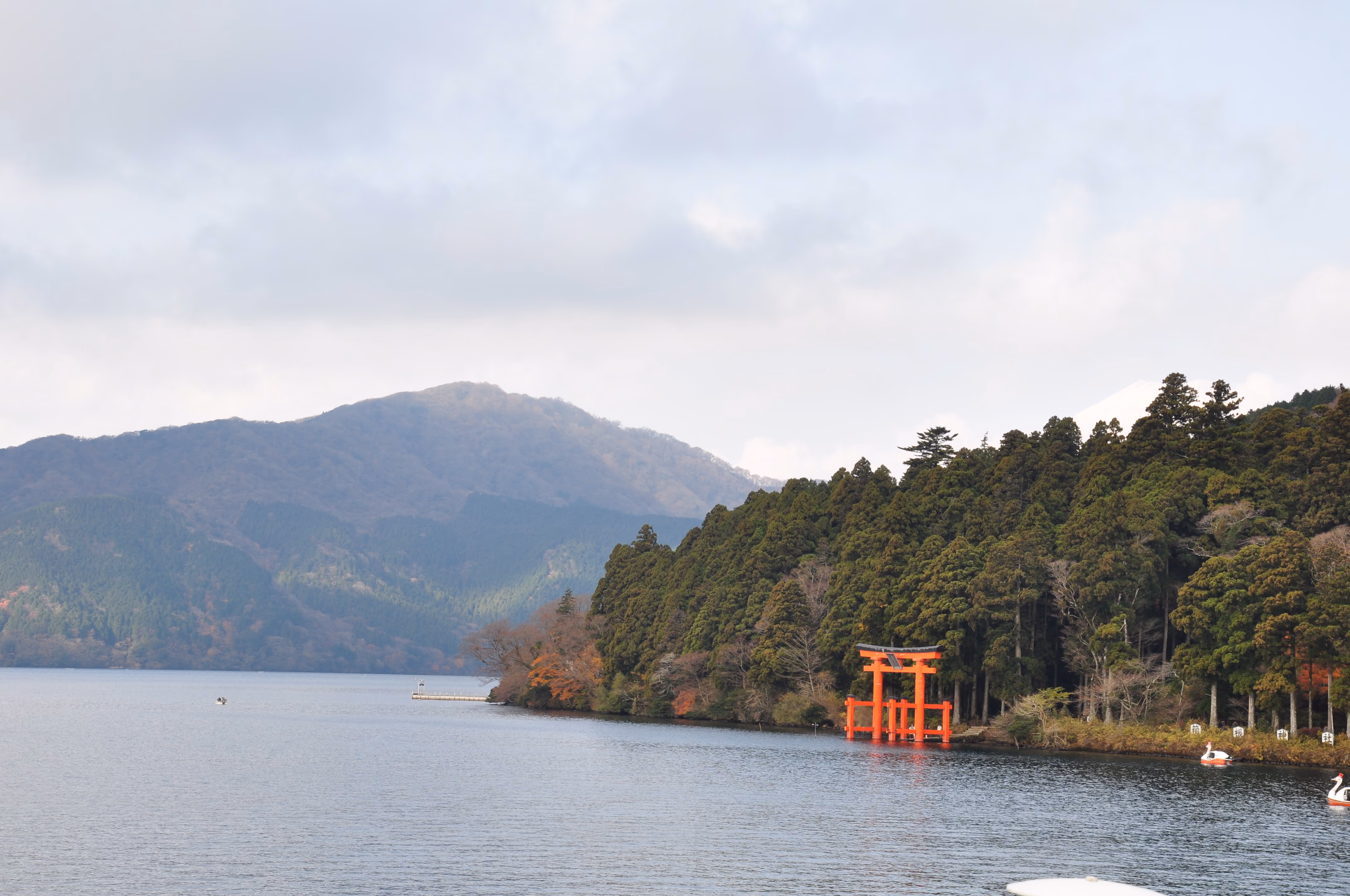 The red torii gate in Lake Ashi with swan-shaped pedal boats in the foreground