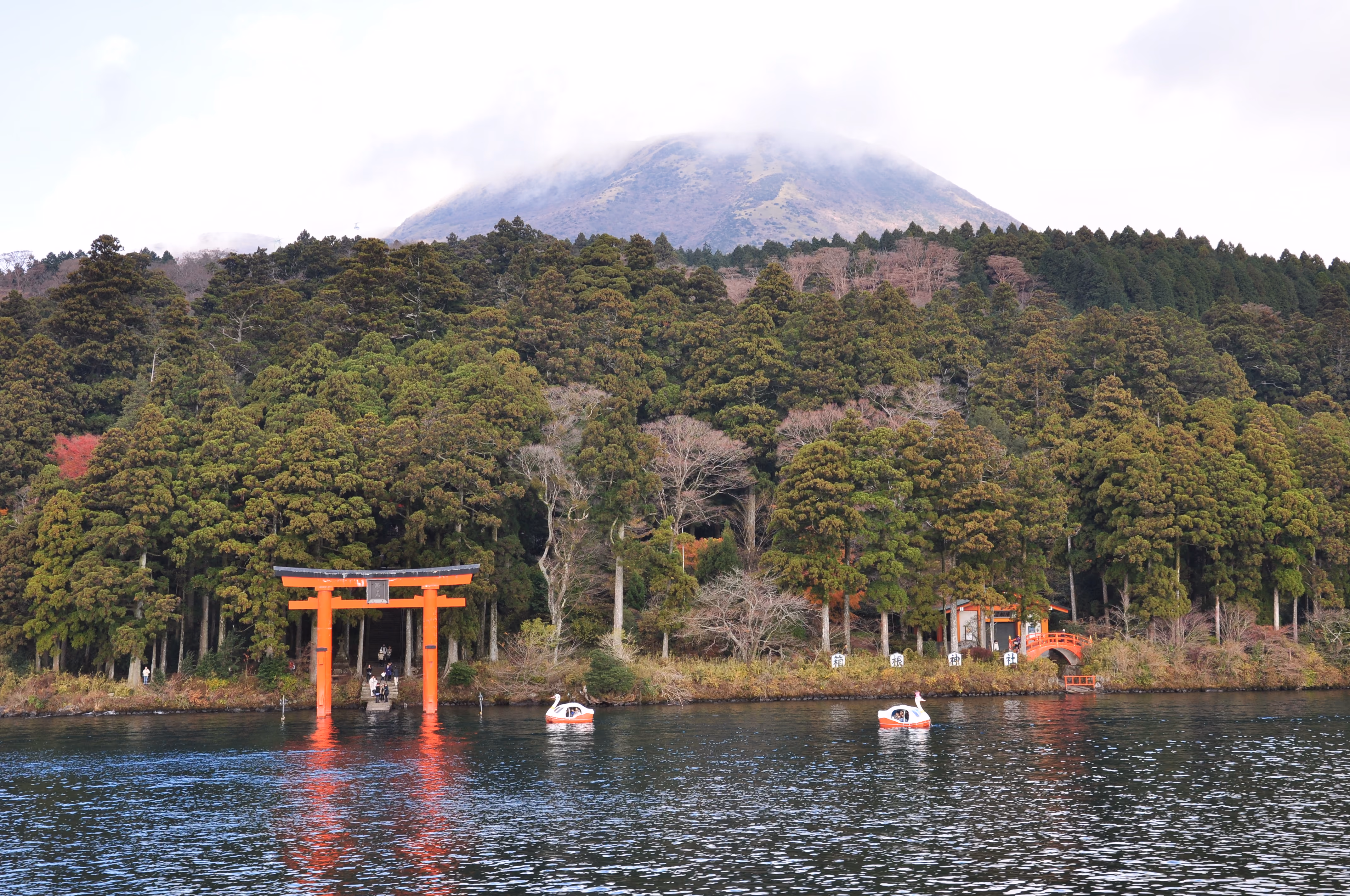 Close view of the red torii gate standing in Lake Ashi, with visitors on the steps behind it