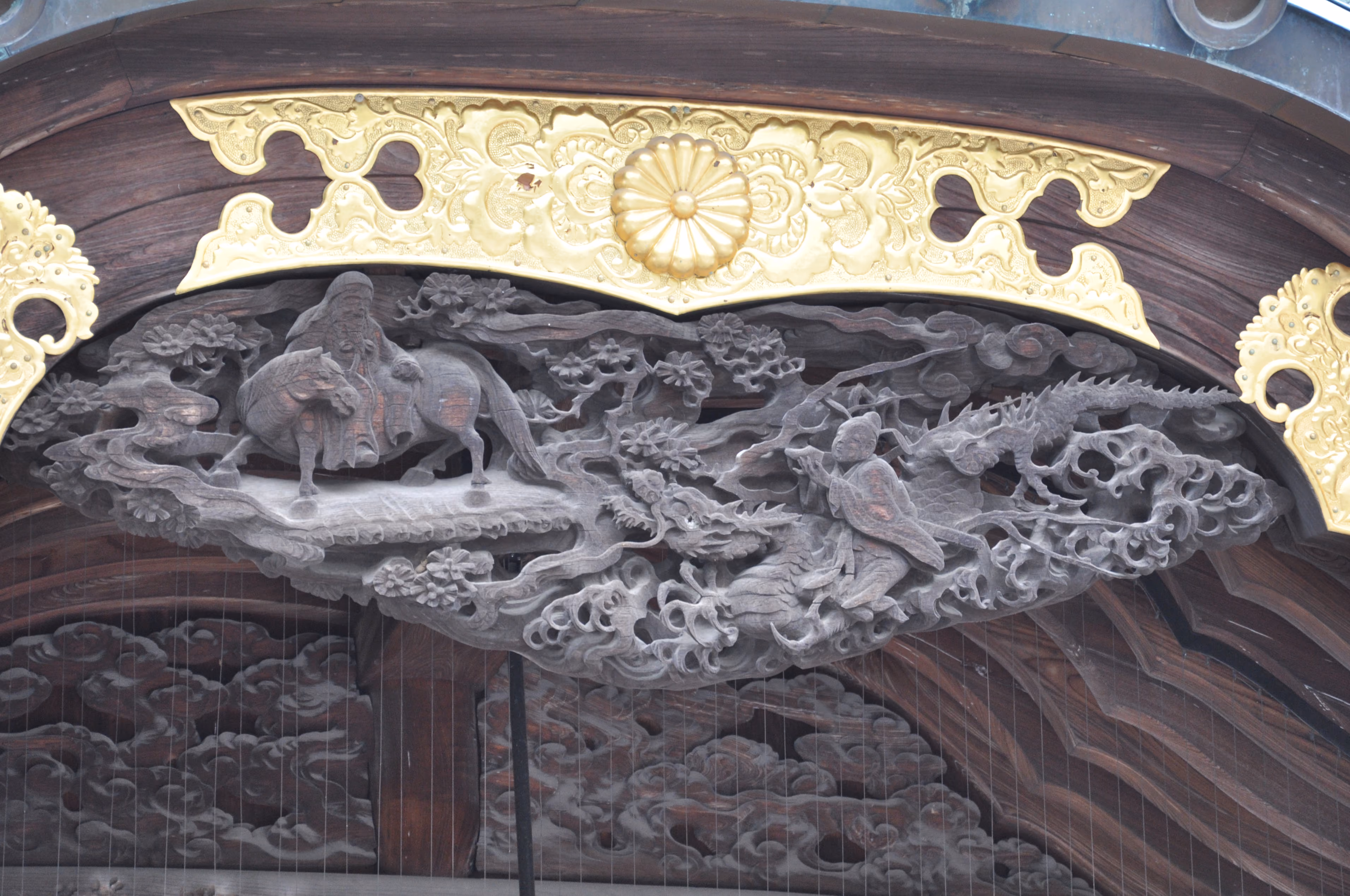 Detailed wood relief carving on Mishima Taisha's main hall, showing a robed figure on horseback and a dragon