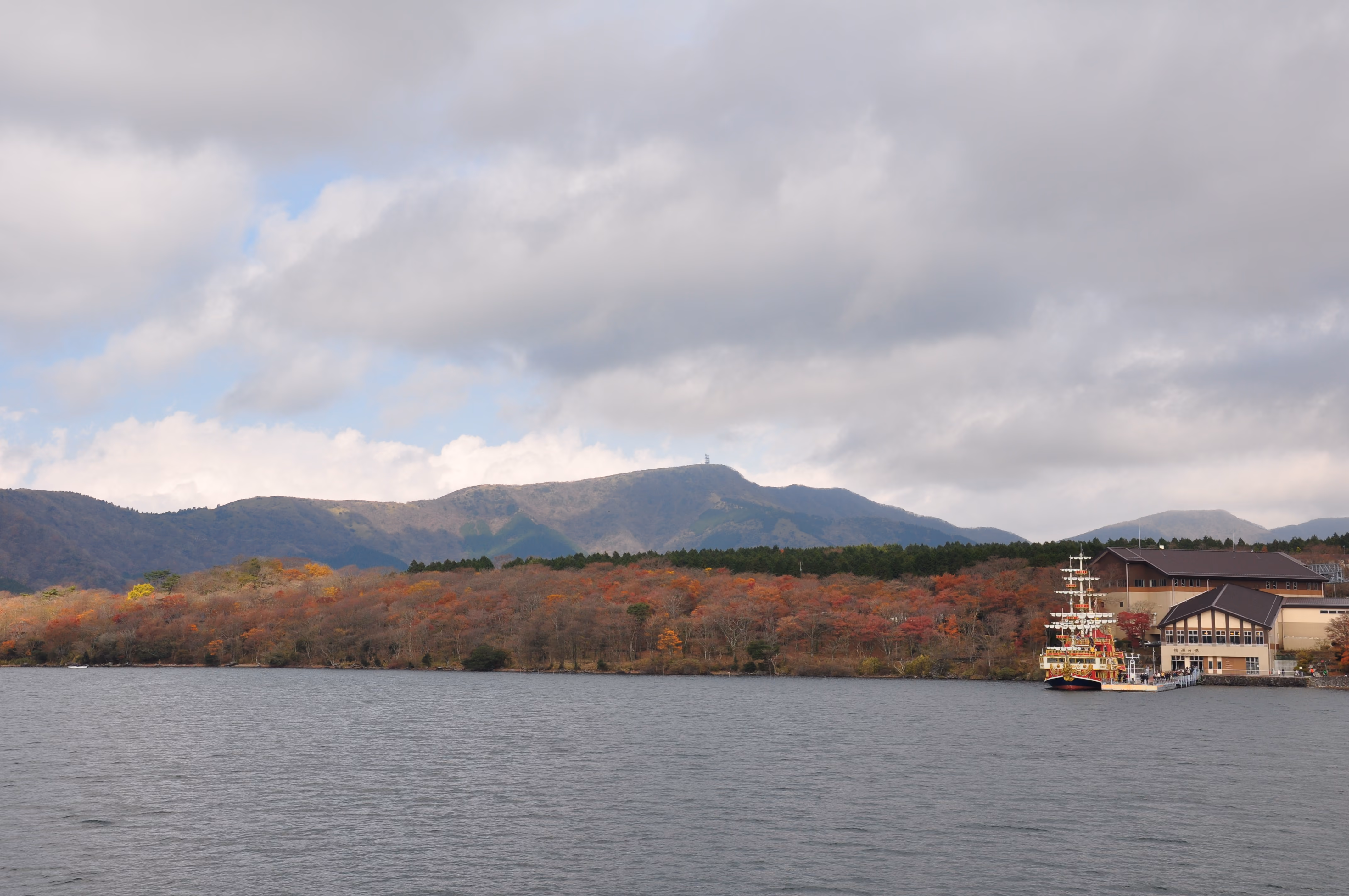 A pirate-ship-styled tour boat docked at a pier at Lake Ashi with autumn foliage on the hillside