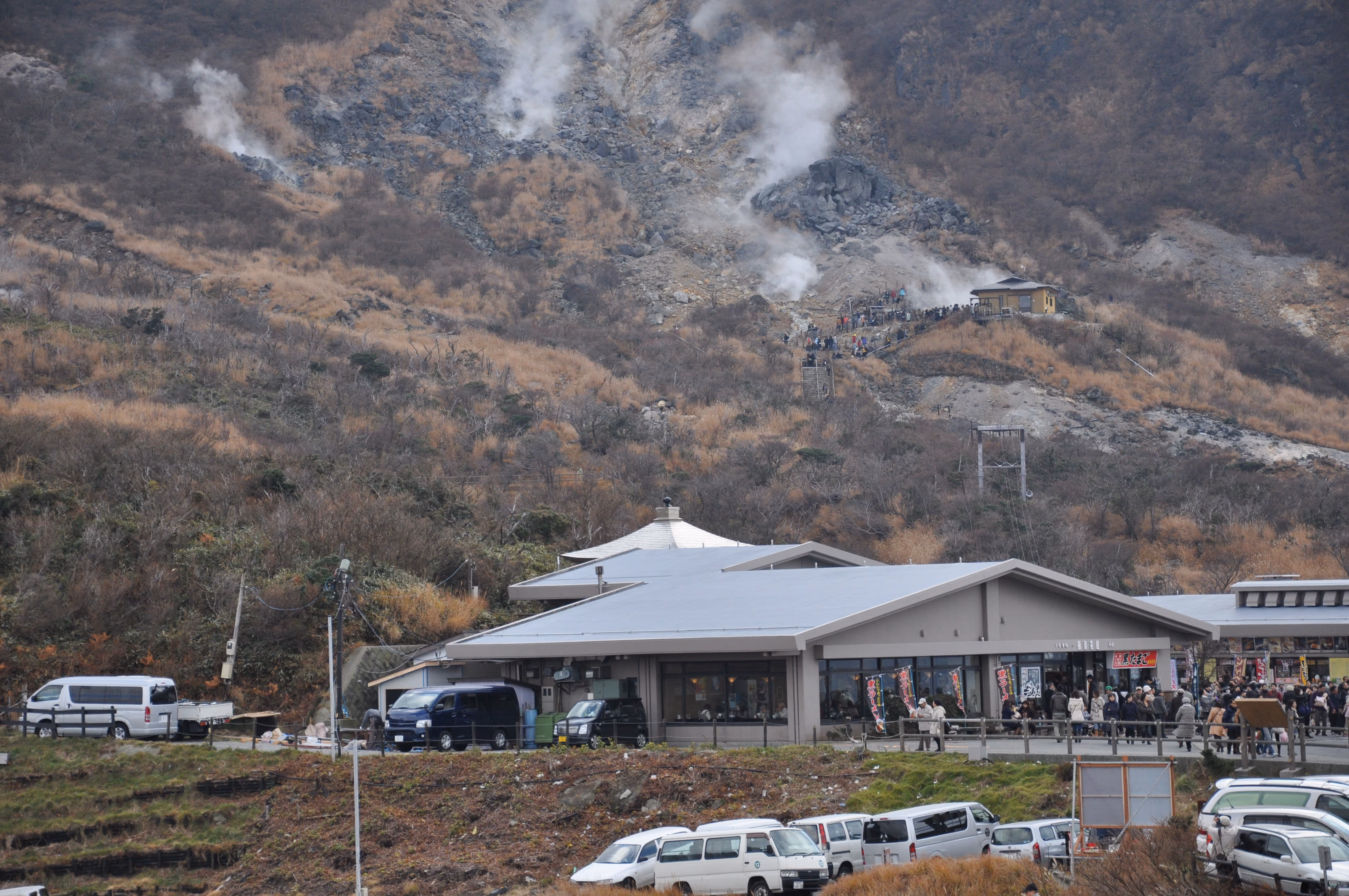 A visitor center building at Owakudani with black ramen banners and a crowd of visitors