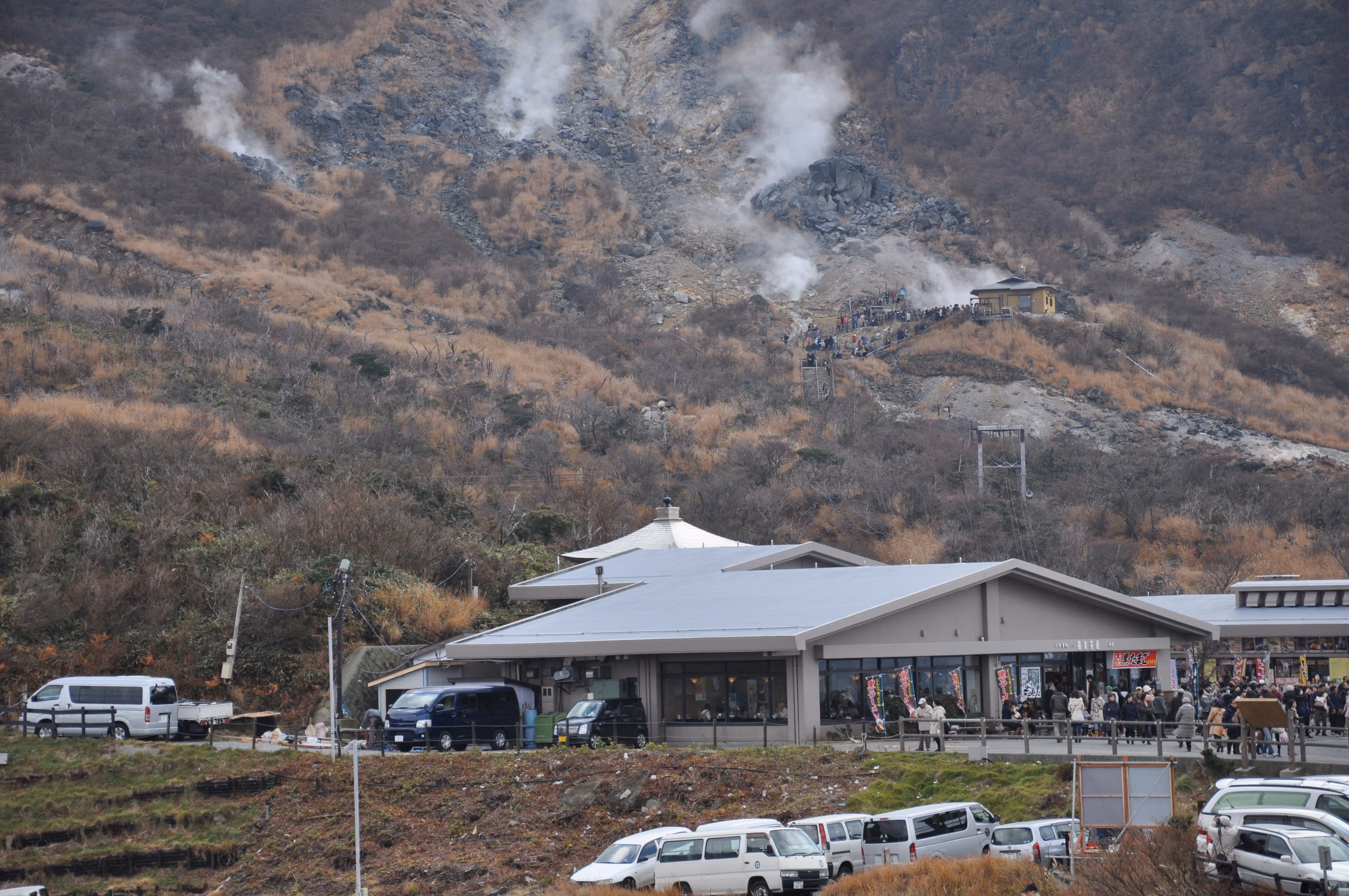 A visitor center building at Owakudani with black ramen banners and a crowd of visitors