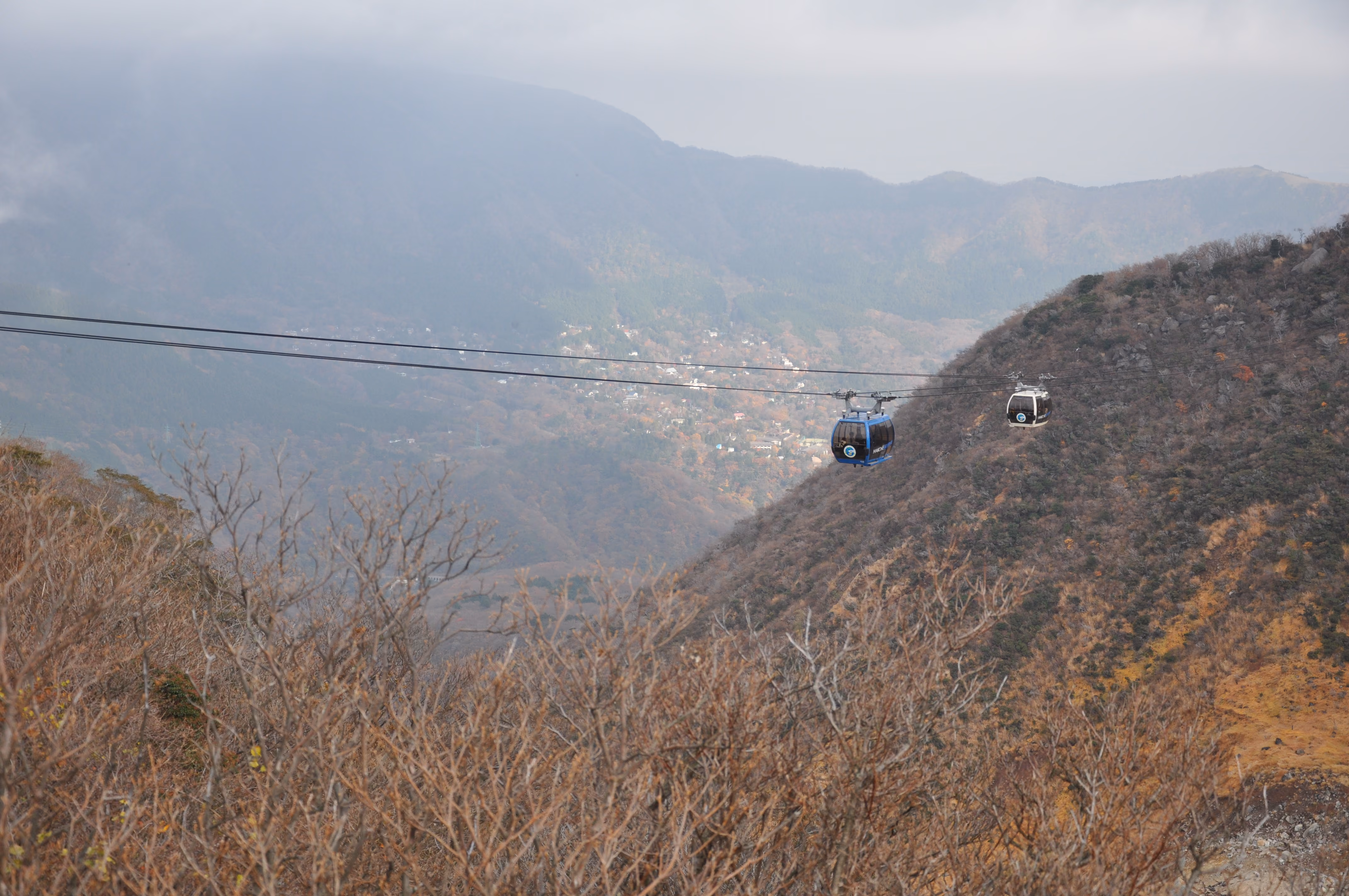 Hakone Ropeway gondolas descending into a valley town surrounded by autumn-colored maple trees