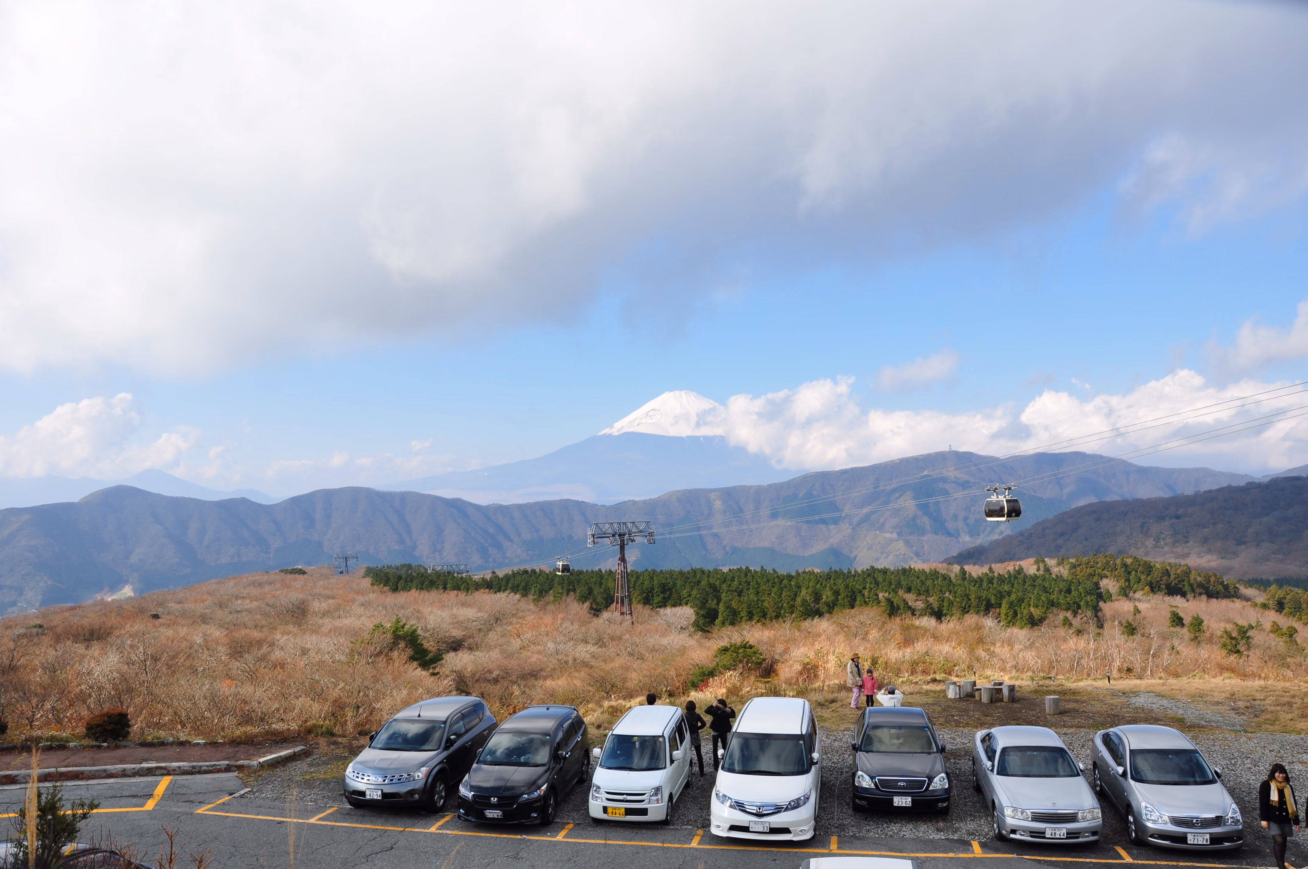 A parking lot at a ropeway station with Mount Fuji visible small in the distance