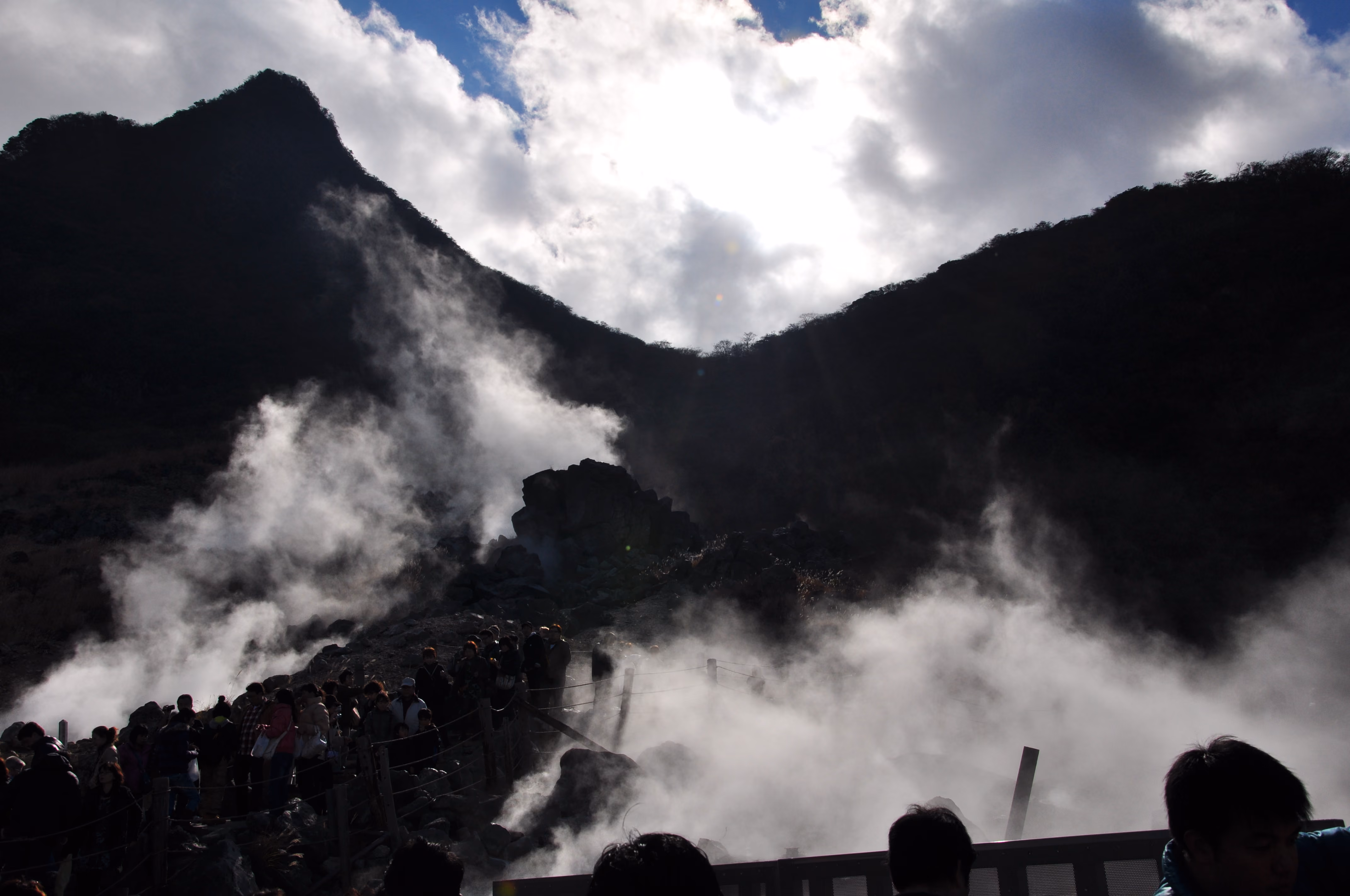Backlit volcanic steam creating dramatic silhouettes of the crater walls at Owakudani, with visitors on a viewing platform below