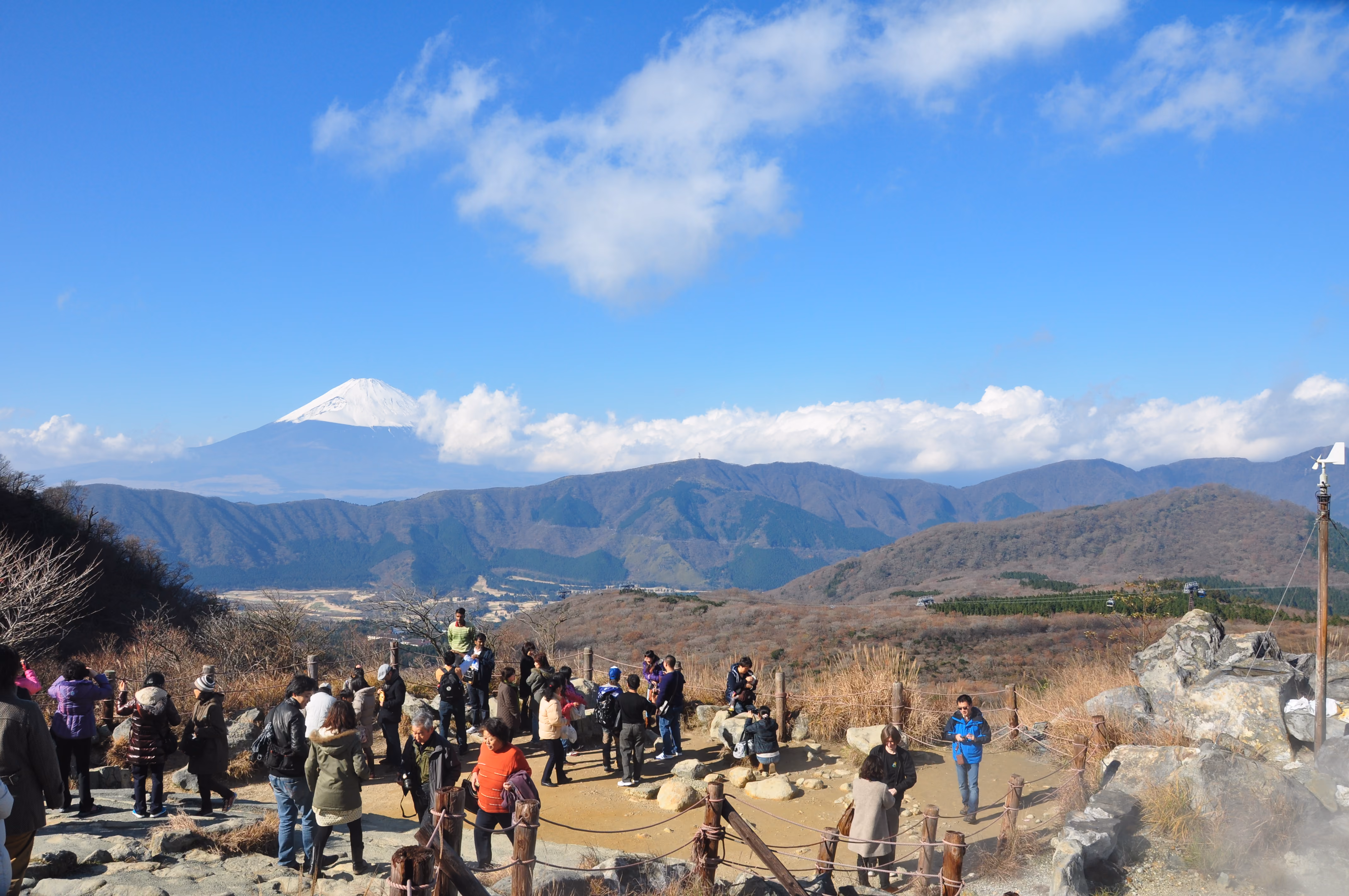 A crowded viewing deck at Owakudani with Mount Fuji visible in the distance