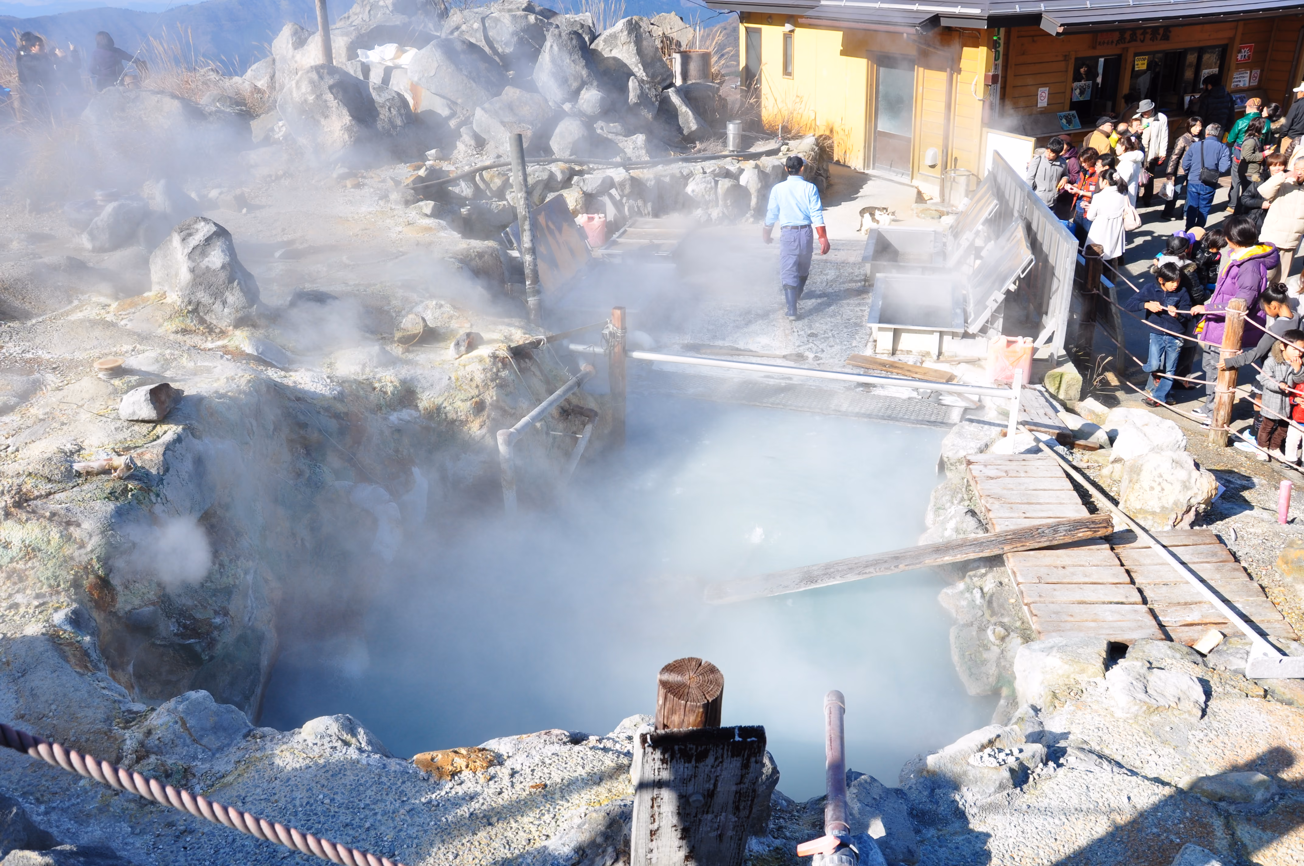 A milky blue-white hot spring pool used for boiling eggs at Owakudani, with a crowd nearby