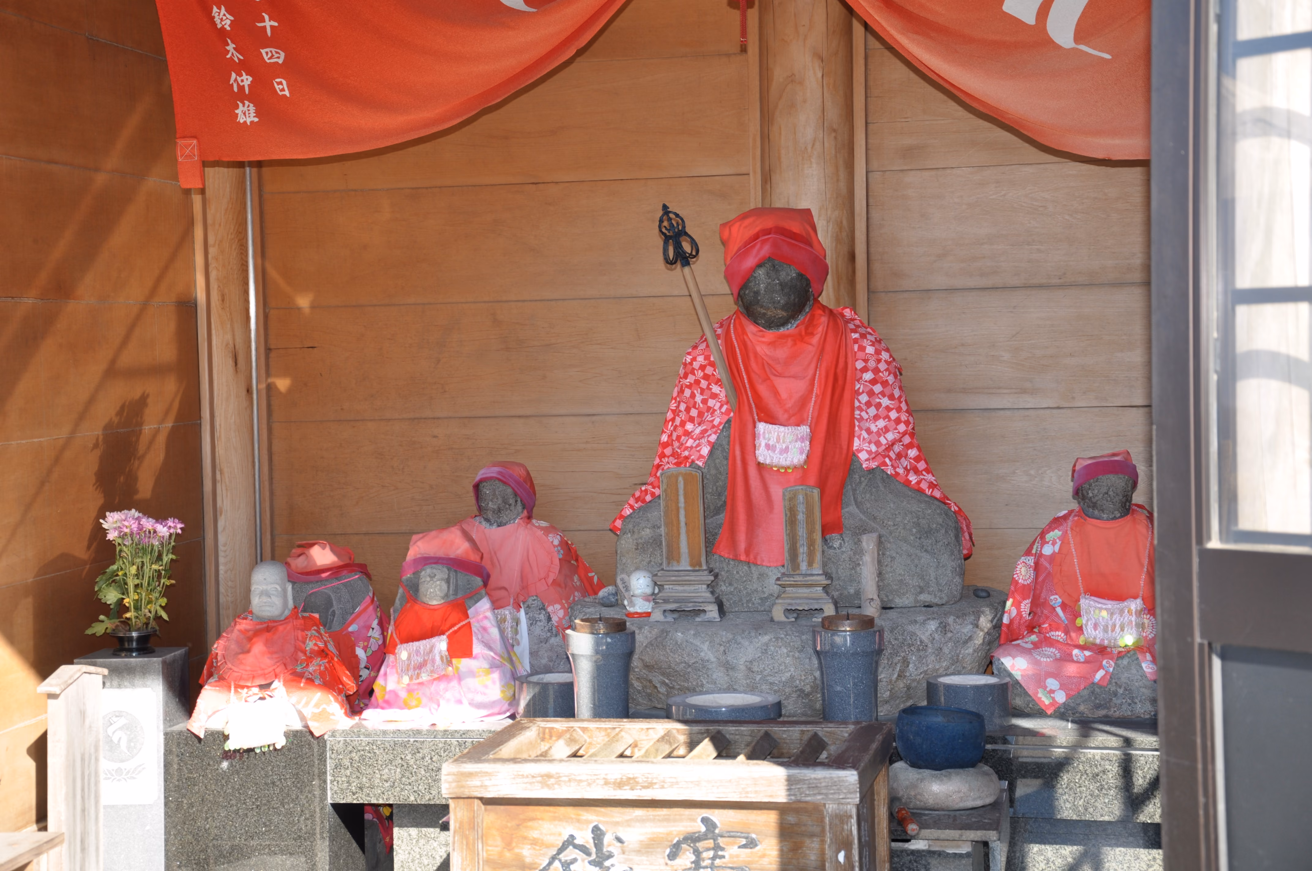 Six small stone Jizo statues wrapped in red cloth inside a small shrine building