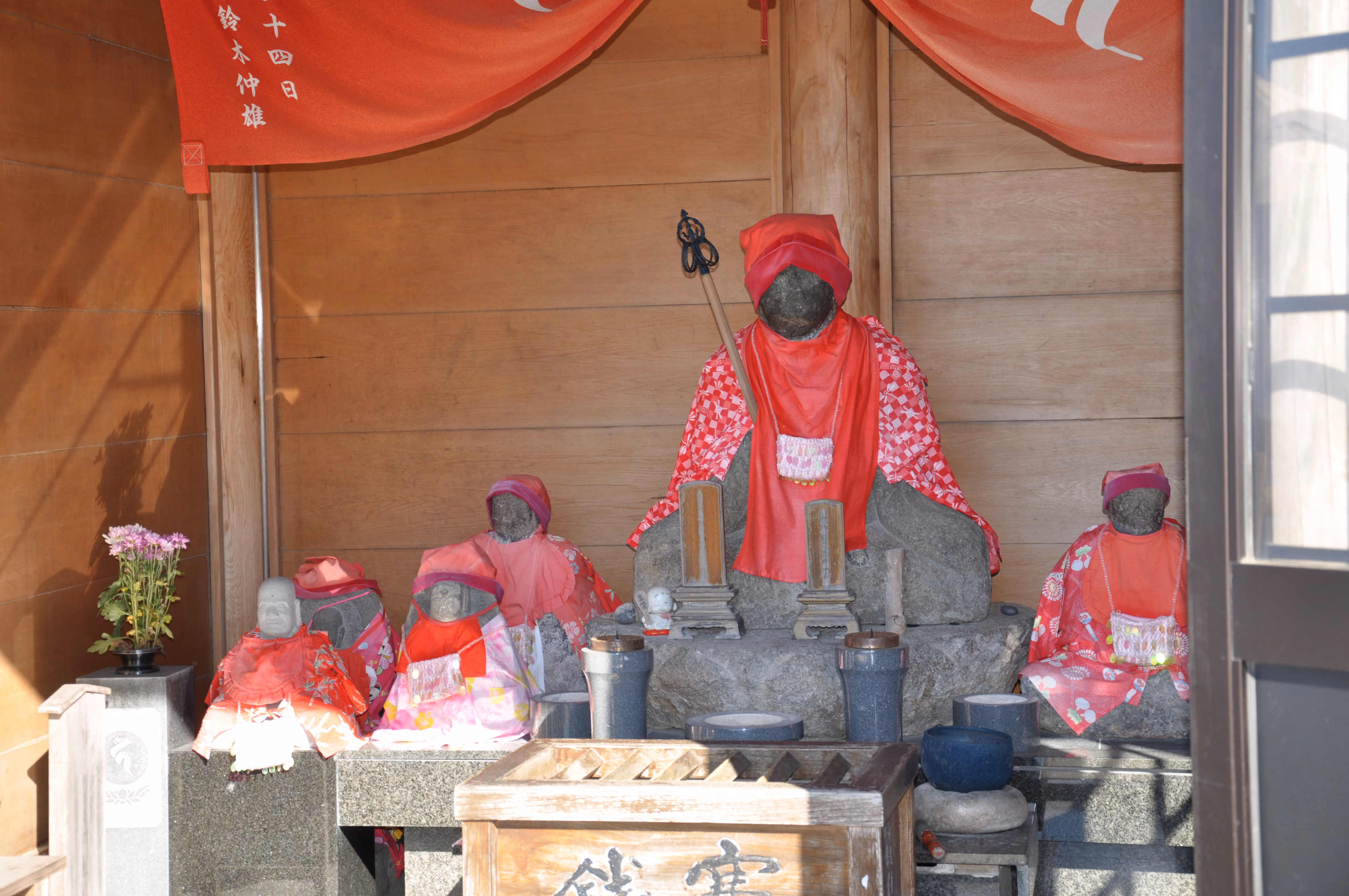 Six small stone Jizo statues wrapped in red cloth inside a small shrine building