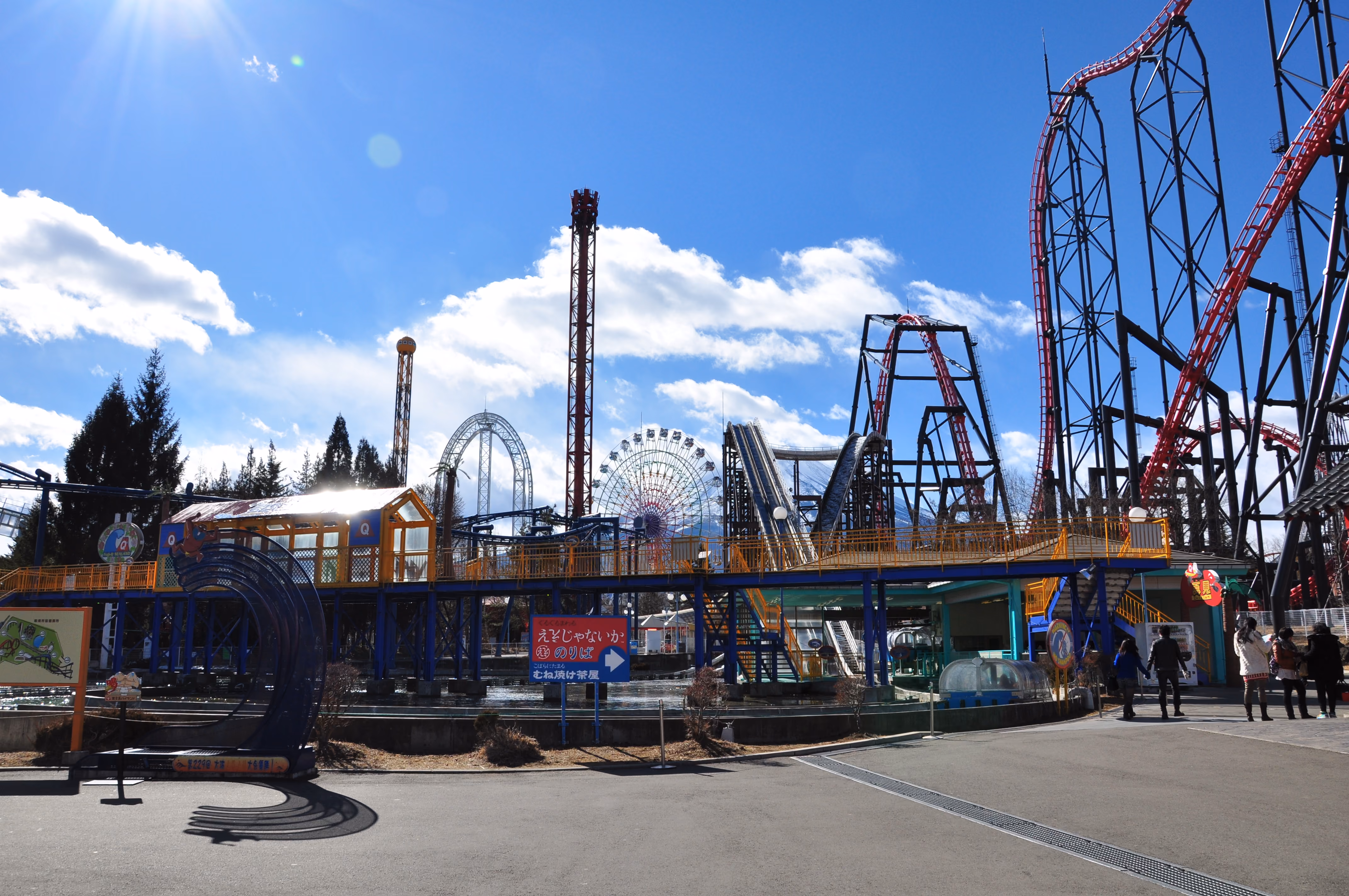 Wide view of Fuji-Q Highland amusement park with multiple roller coasters and a ferris wheel under a clear blue sky