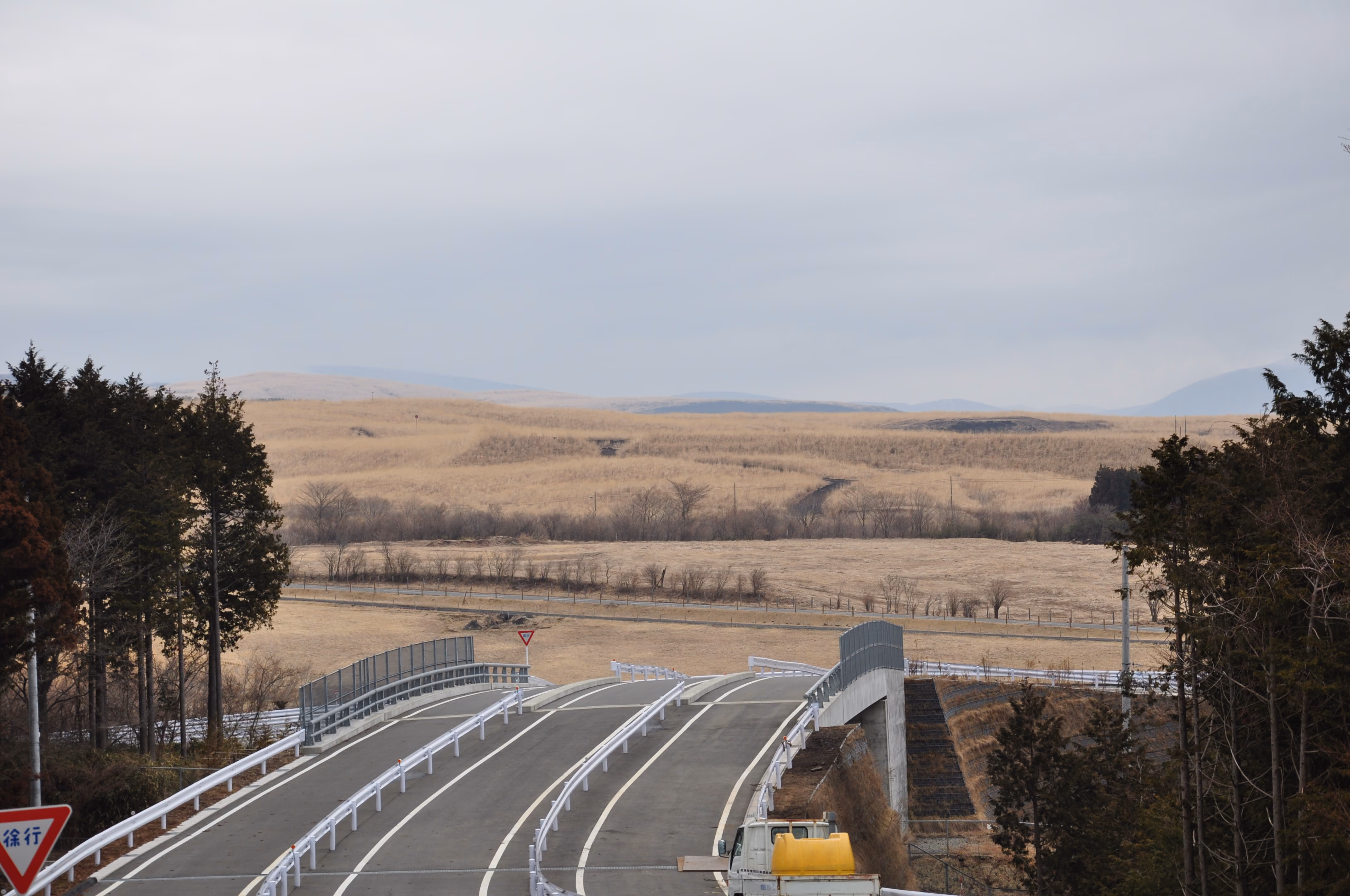 A road curving through dry grassland toward distant hills, near Fuji Safari Park