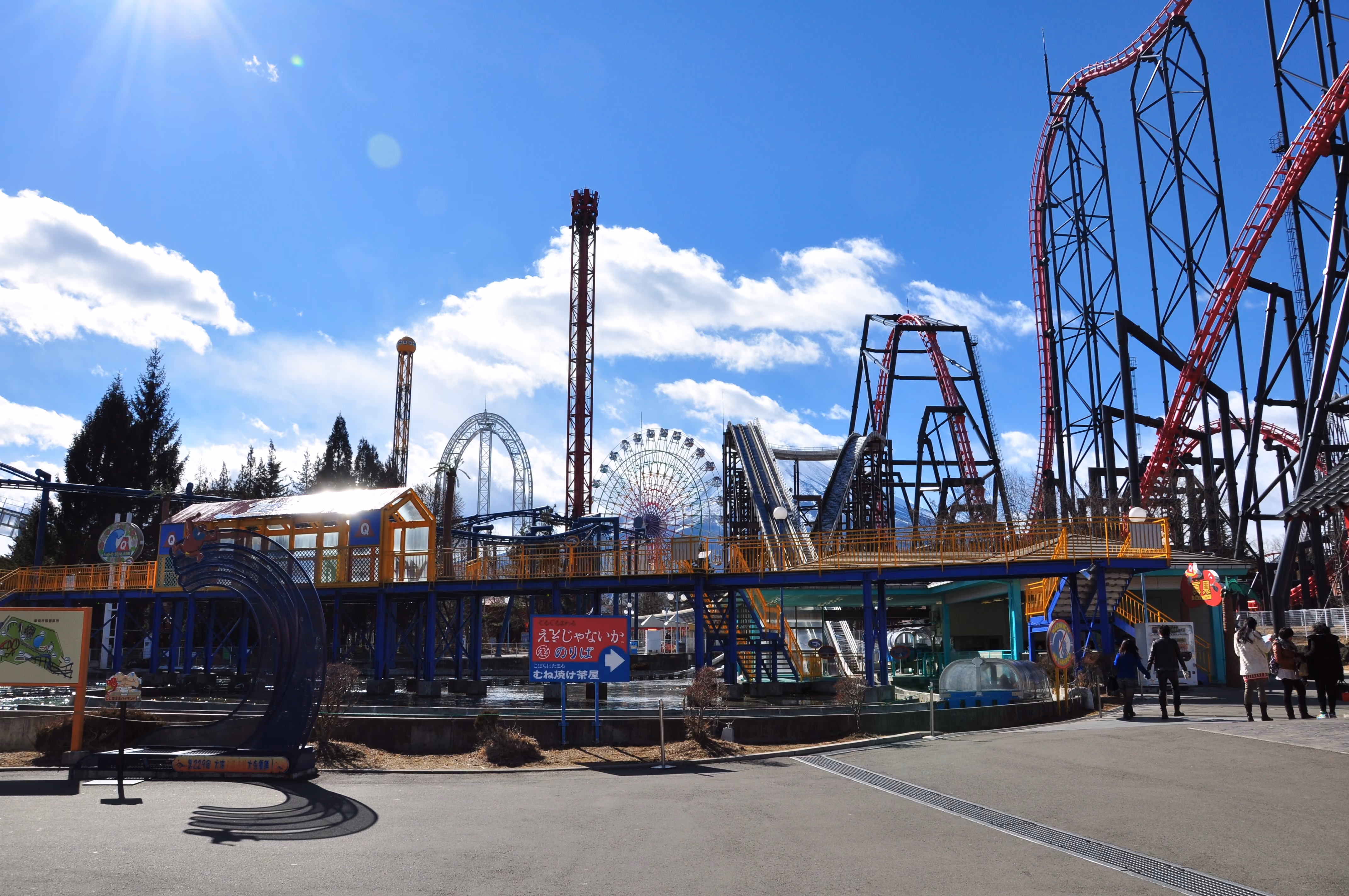 Wide view of Fuji-Q Highland amusement park with multiple roller coasters and a ferris wheel under a clear blue sky