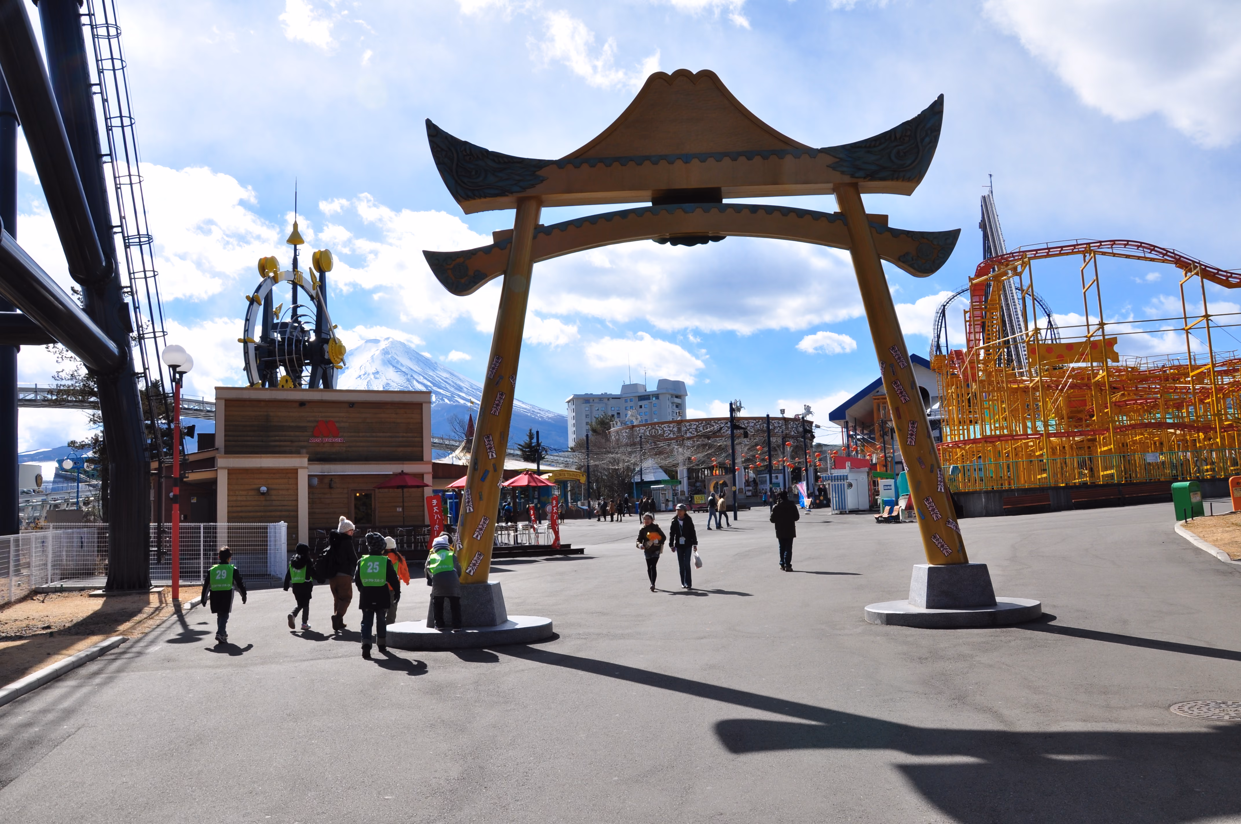 A large wooden torii-style entrance arch at Fuji-Q Highland with Mount Fuji visible in the background and a school group walking through