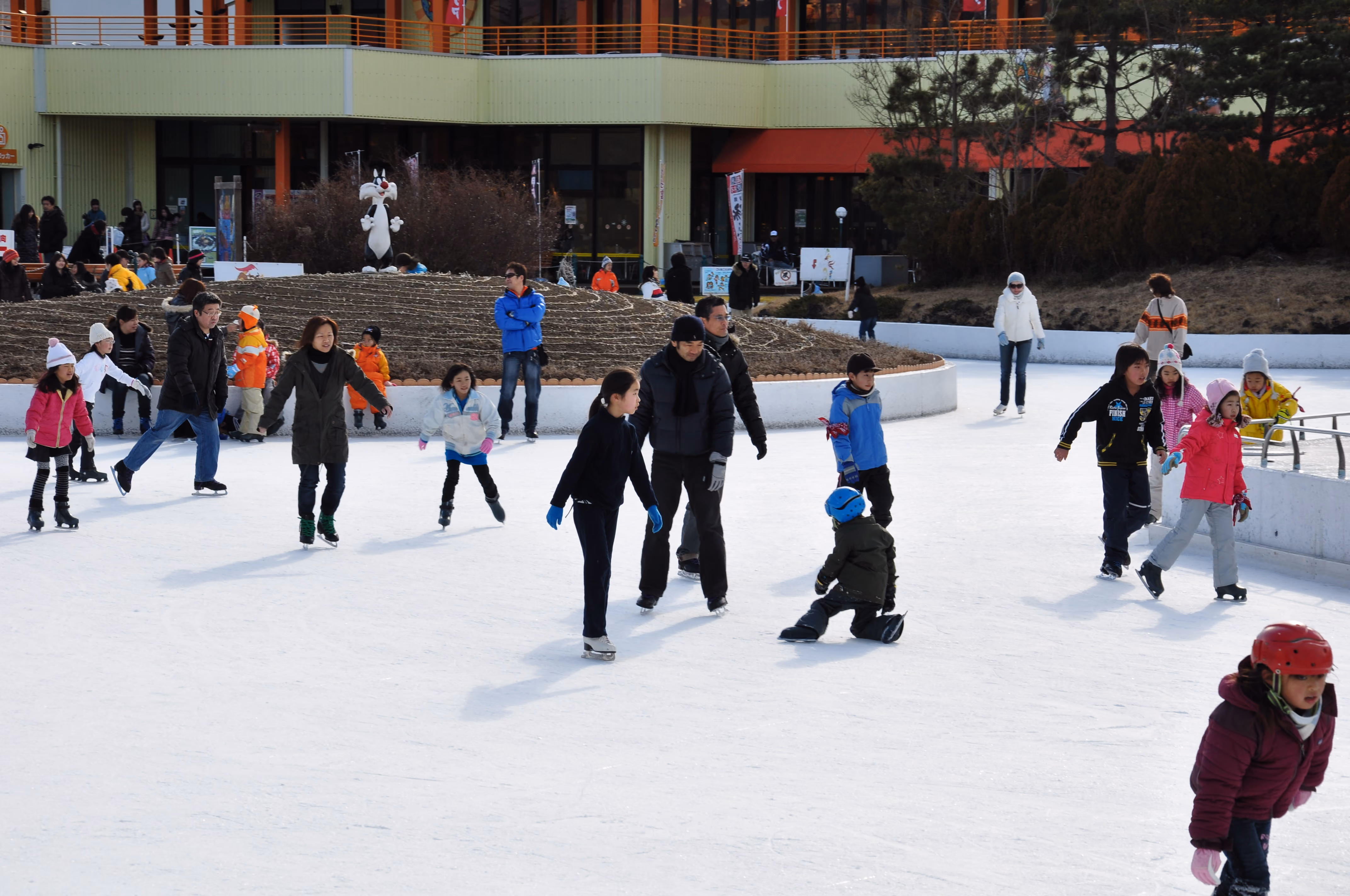 People ice skating on an outdoor rink with Mount Fuji and park buildings visible behind them