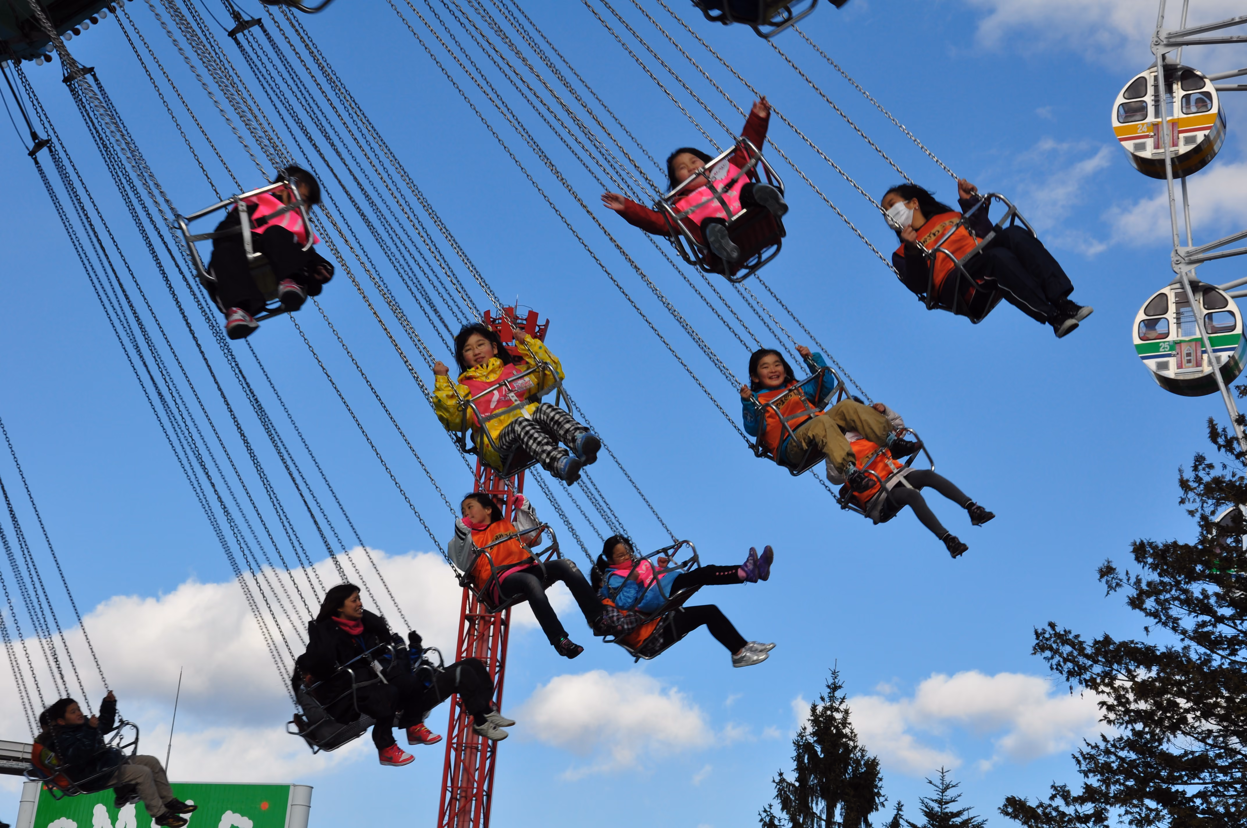 Close-up of children riding a swing carousel, mid-swing against a blue sky