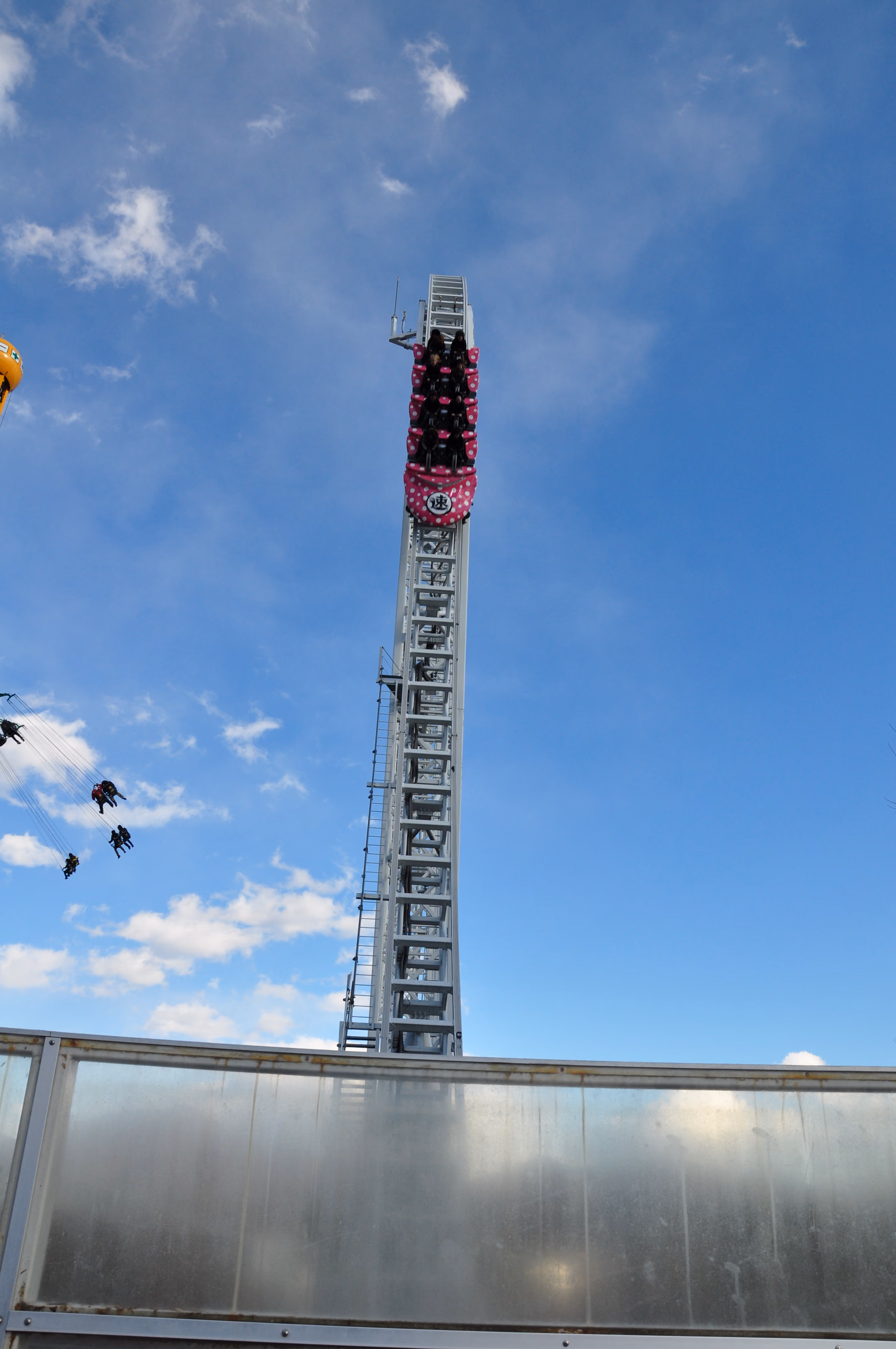 A pink polka-dot roller coaster train climbing a vertical launch tower against a blue sky