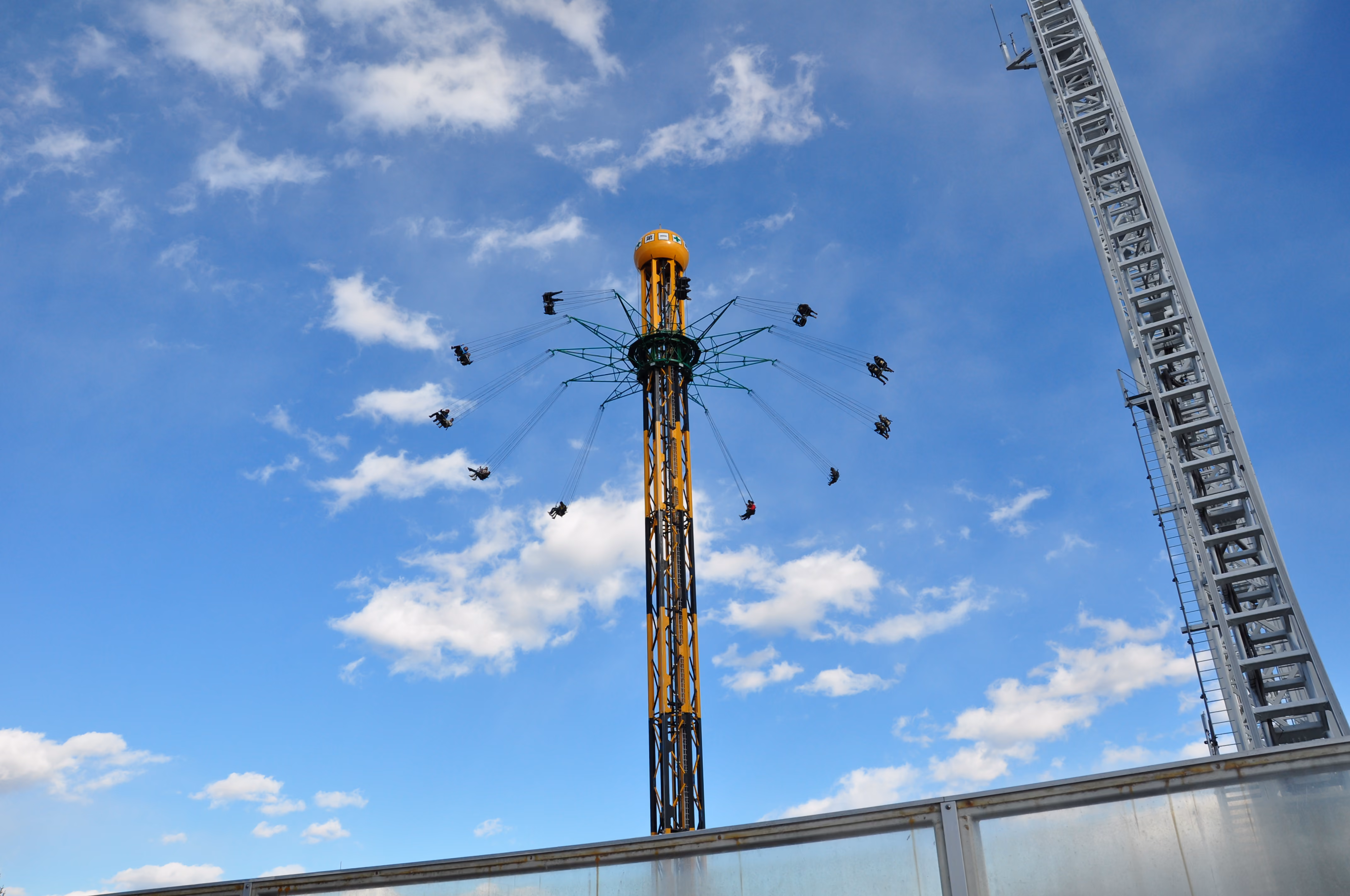 A star flyer swing tower ride with riders suspended at various heights against a blue sky