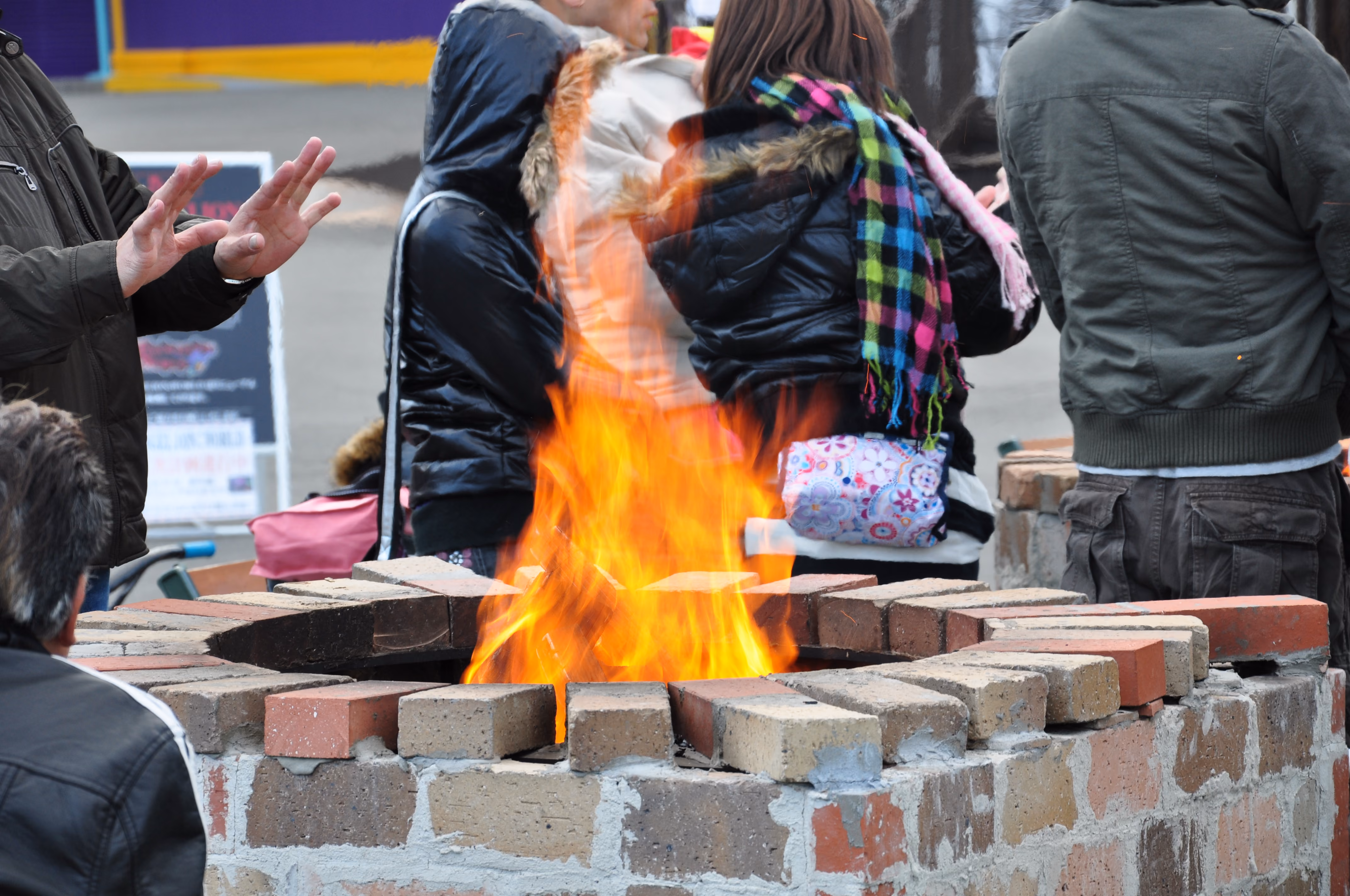 People warming their hands at a brick fire pit at an amusement park