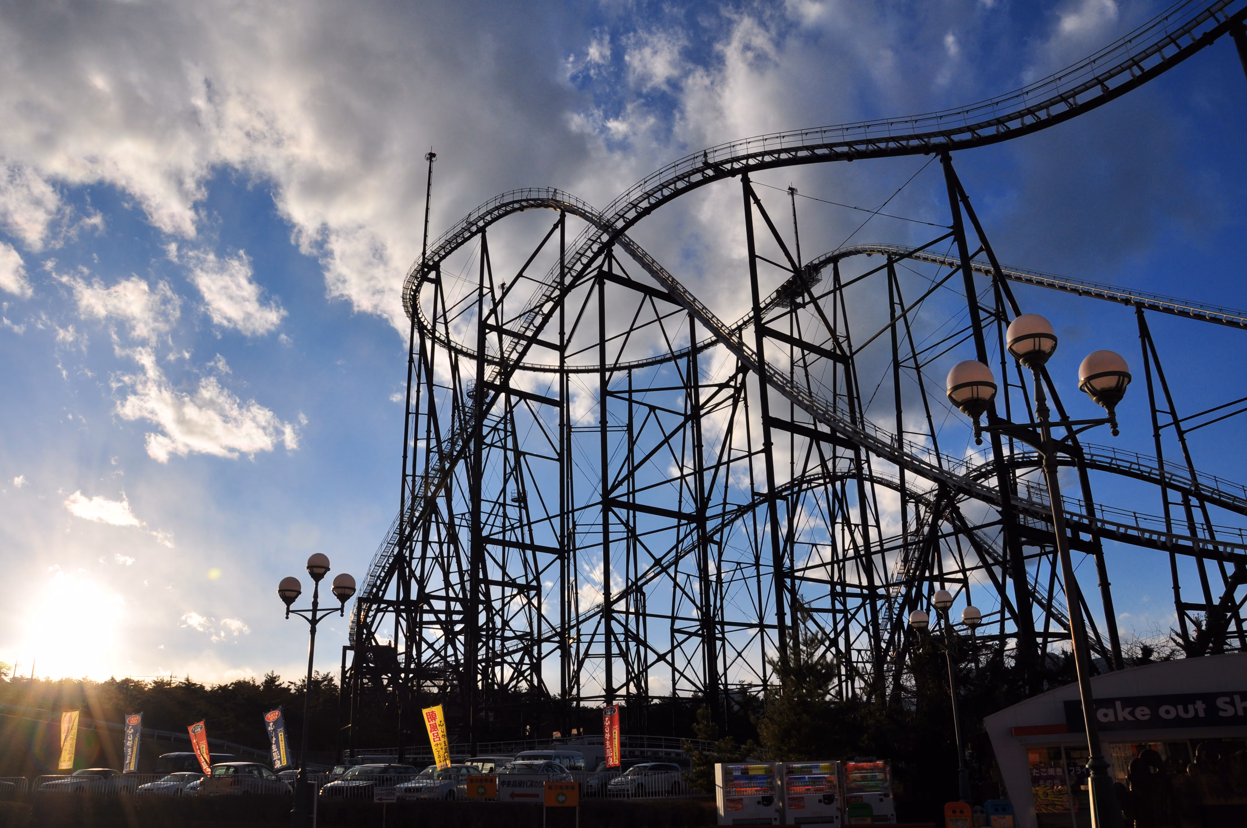 Silhouette of a roller coaster against a sunset sky with lens flare
